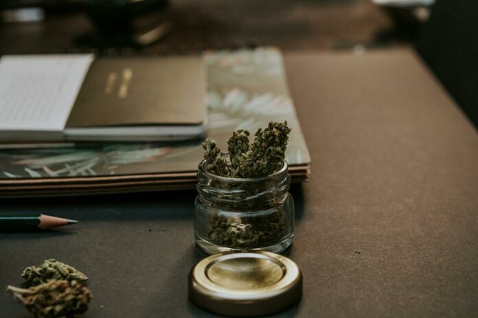 A close-up image of cannabis buds in a glass container on a desk, emphasizing a natural and relaxed setting.